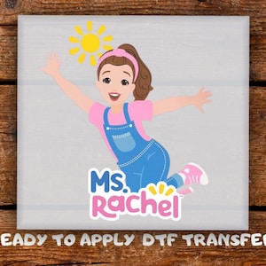 May include: A colourful graphic of a cartoon character, Ms. Rachel, wearing a pink shirt and blue overalls, with a yellow sun. The text "Ms. Rachel" is below the character. The words "READY TO APPLY DTF TRANSFER" are at the bottom.