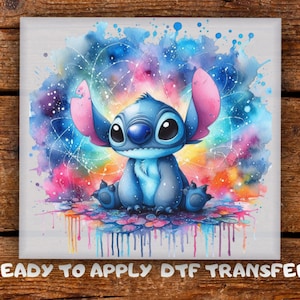 May include: A blue cartoon character with large eyes and ears, set against a vibrant watercolor splash of blues, pinks, and yellows. The image is a ready-to-apply DTF transfer, perfect for crafting projects.