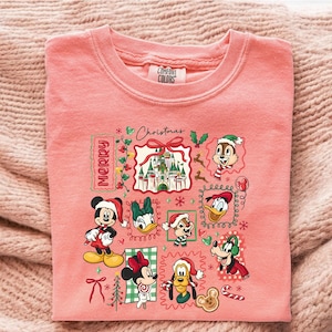 May include: A coral-colored Comfort Colors sweatshirt featuring a festive Disney-themed graphic. The design includes Mickey and Minnie Mouse, Donald Duck, and other characters in Santa hats, with the word "Merry" and "Christmas" displayed.