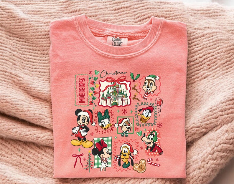 May include: A coral-colored Comfort Colors sweatshirt featuring a festive Disney-themed graphic. The design includes Mickey and Minnie Mouse, Donald Duck, and other characters in Santa hats, with the word "Merry" and "Christmas" displayed.