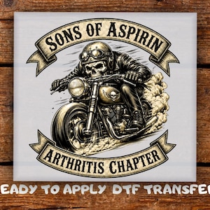 May include: A DTF transfer featuring a graphic of a skull wearing a leather jacket and goggles riding a motorcycle. The text reads SONS OF ASPIRIN at the top and ARTHRITIS CHAPTER at the bottom, with READY TO APPLY DTF TRANSFER printed below.