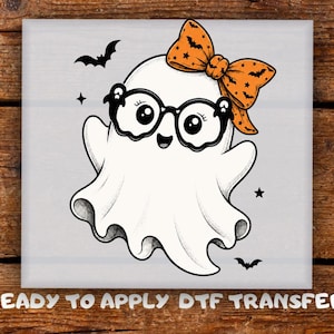 May include: A white ghost graphic with black outlines, wearing black-rimmed glasses and an orange bow with a black bat pattern. The ghost is surrounded by small black bats and stars. The text below reads READY TO APPLY DTF TRANSFER.
