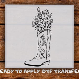 May include: Black and white line art of a cowboy boot filled with flowers. The boot has decorative stitching. The text "READY TO APPLY DTF TRANSFER" is at the bottom of the image. The image is on a light gray background.