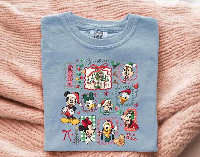 May include: Light blue Comfort Colors t-shirt featuring a Christmas-themed graphic. The design includes the word "Merry" and various Disney characters like Mickey Mouse, Minnie Mouse, Donald Duck, and Chip and Dale, all in festive attire.
