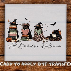 May include: A DTF transfer featuring four black cats reading books, wearing witch hats, and surrounded by pumpkins, a skull, and bats. The text reads All Booked for Halloween and Ready to Apply DTF Transfer. The design includes colorful book spines.