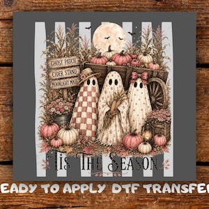 May include: A graphic design featuring three ghosts standing in front of a wooden wagon, pumpkins, and corn stalks. A sign reads GHOST PATCH, CIDER STAND, MOONLIGHT MAZE. The text TIS THE SEASON is at the bottom. The ghosts wear hats and bows.
