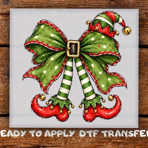 May include: A festive graphic design featuring a large green polka-dot bow with a central black buckle, topped with a red and green elf hat with a gold bell. Two striped green and white elf legs with red curled shoes hang below.