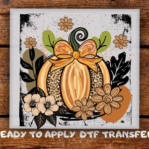 May include: A square DTF transfer featuring a pumpkin design with a leopard print center, adorned with a yellow bow, flowers, and leaves. The text "READY TO APPLY DTF TRANSFER" is at the bottom. The design has a distressed, vintage look.