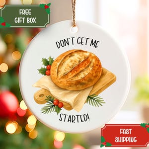 May include: White ceramic ornament with a bread design. The ornament features a round loaf of bread on a wooden cutting board with the text "DON'T GET ME STARTED!" and holly accents. A gold string is attached for hanging.