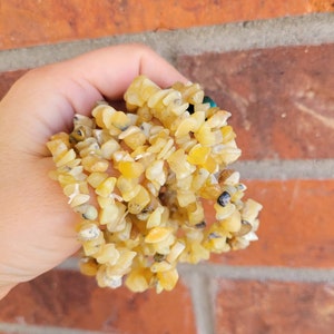 May include: A strand of yellow chip gemstone beads. The beads are irregular in shape and have a natural, rough texture.