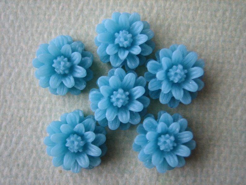 K&ouml;nnte beinhalten: Sechs blaue, blumenf&ouml;rmige Cabochons. Die Cabochons sind aus Harz und haben eine gl&auml;nzende Oberfl&auml;che.