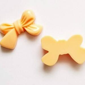 May include: Two peach-colored plastic bows. One bow is tied with a knot in the center, and the other bow is flat.