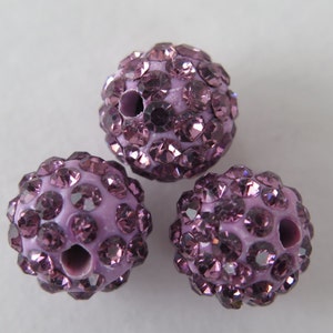 May include: Three purple round beads with a hole in the center. The beads are covered in small, sparkly rhinestones.