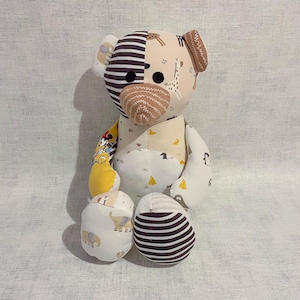 May include: A patchwork teddy bear made from various patterned fabrics. The bear has black and white stripes, giraffe print, and other colourful designs. It has black button eyes and a stitched nose.