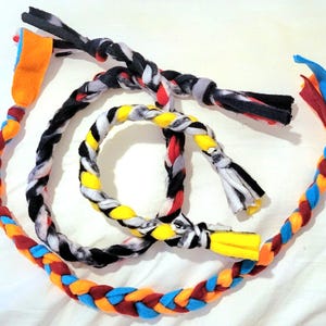 May include: Three braided dog toys made from colorful fleece fabric. The toys are in various colors, including red, blue, yellow, orange, black, and white.