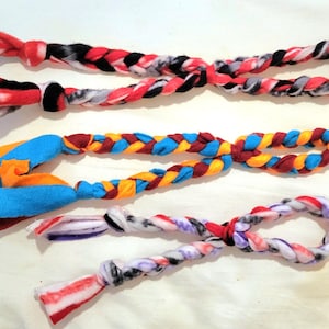 May include: Three braided dog toys made from colorful fabric scraps. The toys are in various colors, including red, black, white, blue, yellow, and purple.