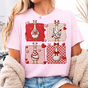 Könnte beinhalten: Hellrosa T-Shirt mit vier quadratischen Designs mit Cartoon-Gänsen. Jede Gans ist mit Herzen, Schleifen und Amor-Motiven geschmückt, um den Valentinstag zu feiern. Das T-Shirt besteht aus einem weichen Material.