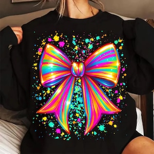 May include: Black sweatshirt featuring a vibrant, multi-colored bow graphic. The bow design incorporates shades of pink, blue, yellow, and green, with a splash effect background. The sweatshirt is a casual, comfortable garment.