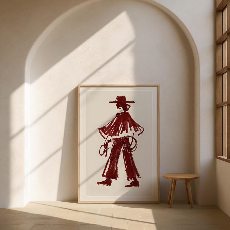 May include: A framed illustration of a person wearing a wide-brimmed hat and a long, flowing cape. The person is standing with their arms at their sides, and they are holding a rope in their right hand. The illustration is done in a red color and is set against a white background.