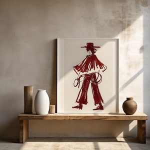 May include: A framed illustration of a person wearing a hat and a long, flowing red garment. The illustration is on a white background and is framed in a simple black frame. The illustration is hanging on a wall with a wooden shelf below it.