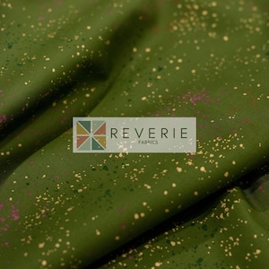 May include: Olive green fabric featuring a scattered pattern of metallic gold and dark purple paint splatters. The fabric is draped in soft folds and includes a rectangular logo overlay with the text REVERIE FABRICS and a geometric icon.
