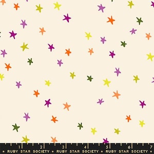 May include: A cream-colored fabric featuring a scattered pattern of hand-drawn stars in orange, purple, lime green, and dark olive green. A black ruler at the bottom shows measurements in inches, with the text Ruby Star Society printed repeatedly.