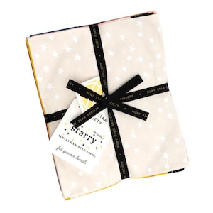 May include: A bundle of fabric fat quarters tied with a black ribbon. The fabric is cream-colored with white star patterns. A tag with the word "starry" is attached to the ribbon. The bundle is labeled "fat quarter bundle."