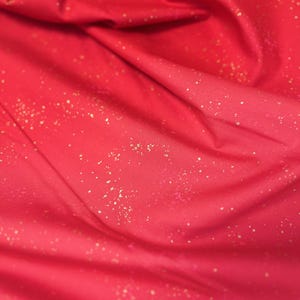 May include: Close-up of a vibrant red fabric with a subtle gradient effect. The material is adorned with scattered gold flecks, creating a shimmering, textured appearance. The fabric is draped, showing folds and shadows.