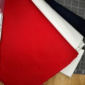 May include: A Moda Remnant Bag #11 containing folded fabric pieces in solid red, white, and dark navy blue. The clear plastic packaging features a white label with the text Moda Remnant Bag Solids and the weight of 2 lb 12 oz.