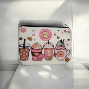 May include: A rectangular, off-white zippered pouch featuring a coffee-themed design. The design includes four different coffee drinks, pastries, and the text "CAFECITO Y CHISME" in a pink circle. The pouch has a black zipper.