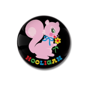 May include: A round, black button with a pink squirrel holding a yellow flower. The squirrel has a blue bow and the word "HOOLIGAN" is written in colorful letters around the bottom of the button.