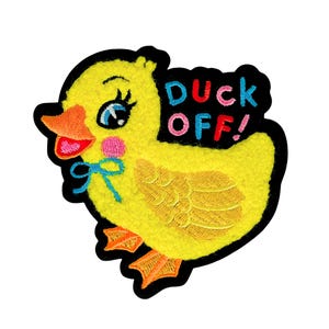May include: Embroidered yellow duck patch with a black border. The duck has a pink cheek, blue bow, and the text "DUCK OFF!" in red, pink, and blue. The duck's beak and feet are orange.