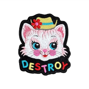 May include: Embroidered patch featuring a white cat face with blue eyes, pink cheeks, and a yellow hat with a red flower. The word "DESTROY" is embroidered in colorful letters on a black background.