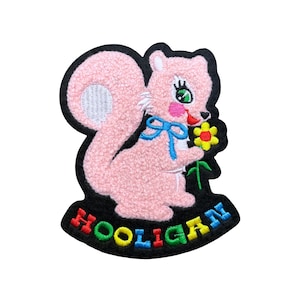 May include: Embroidered patch featuring a pink squirrel holding a yellow flower with green stem. The squirrel has a blue bow and a black outline. The word "HOOLIGAN" is in colorful letters at the bottom. The patch is on a white background.