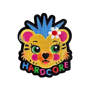 May include: Embroidered patch featuring a cartoon bear with a blue mohawk, a flower, and a piercing. The bear has green eyes, pink cheeks, and the word "HARDCORE" in rainbow colors. The patch has a black border.