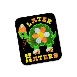 May include: Embroidered patch featuring a green turtle wearing a flower hat and roller skates. The turtle has a flower-shaped shell. The text "LATER HATERS" is in yellow and orange on a black background.