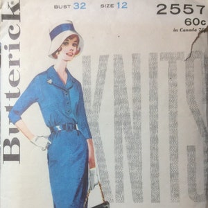 May include: A vintage sewing pattern for a blue dress with a white collar and belt. The pattern is for size 12 and bust 32. The pattern number is 2557 and the price is 60 pence. The pattern is for knit fabric.