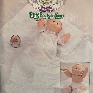 May include: A vintage Cabbage Patch Kids sewing pattern for a preemie doll. The pattern is for a white dress with lace trim and a bonnet. The pattern is from Butterick and is number 373.