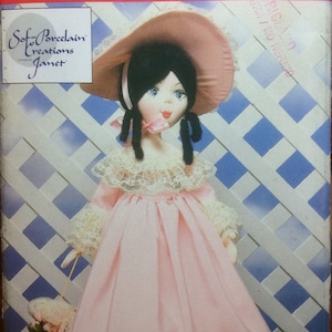 May include: A vintage sewing pattern for a porcelain doll with a pink dress and a wide-brimmed hat. The pattern is from Butterick and is number 3606. The doll is wearing a pink dress with lace trim and a white lace hat.