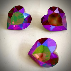 May include: Three iridescent heart-shaped rhinestones with a purple and red colour scheme.