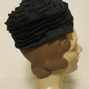 Puede incluir: Un sombrero de tela negro con un dise&ntilde;o de volantes. El sombrero se lleva en la cabeza de un maniqu&iacute;.