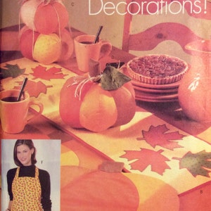 May include: A vintage sewing pattern for Halloween decorations. The pattern includes instructions for making a pumpkin-shaped cushion, a table runner with autumn leaves, and an apron with a pumpkin design. The pattern is from Butterick and has the number 5664.