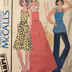 May include: Vintage McCall's sewing pattern envelope with illustrations of three aprons. The aprons are in different styles and colours, including a yellow floral print, a solid red, and a blue denim apron. The envelope includes the text "Carefree Patterns" and "Misses' Butcher Apron."