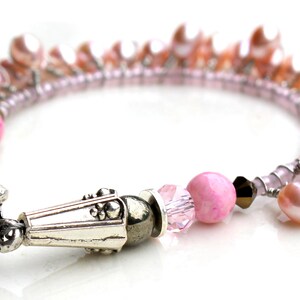 Puede incluir: Una pulsera de perlas rosas con un cierre plateado. La pulsera presenta una mezcla de perlas rosas, cuentas rosas y cristales transparentes. El cierre tiene un dise&ntilde;o ornamentado.