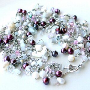 May include: A silver chain necklace with a variety of white, pink, and purple beads. The necklace features a heart-shaped charm and a lobster clasp.