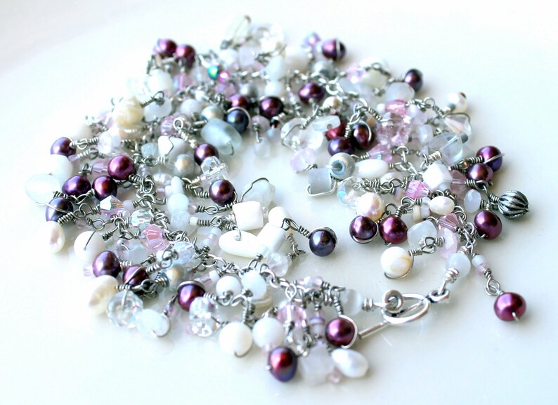 May include: A silver chain necklace with a variety of white, pink, and purple beads. The necklace features a heart-shaped charm and a lobster clasp.