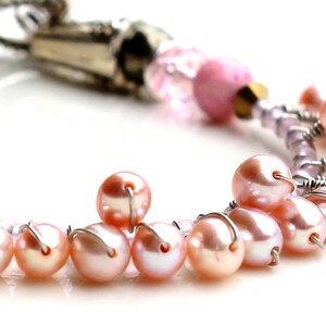 Puede incluir: Primer plano de una pulsera con perlas rosas y detalles met&aacute;licos plateados. La pulsera tiene un dise&ntilde;o delicado con peque&ntilde;as perlas redondas ensartadas con alambre. El fondo es blanco, resaltando la joyer&iacute;a.