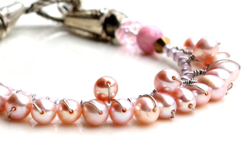 Puede incluir: Primer plano de una pulsera con perlas rosas y detalles met&aacute;licos plateados. La pulsera tiene un dise&ntilde;o delicado con peque&ntilde;as perlas redondas ensartadas con alambre. El fondo es blanco, resaltando la joyer&iacute;a.