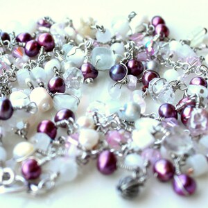 May include: A silver chain necklace with a variety of beads, including white, pink, and purple. The beads are made of different materials, including glass, crystal, and metal.