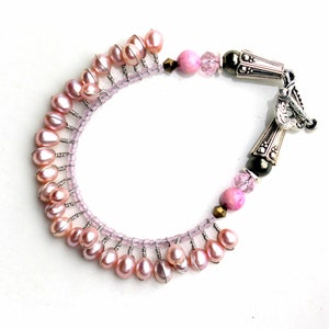 Puede incluir: Una pulsera artesanal con perlas rosas de agua dulce, peque&ntilde;as cuentas rosas y detalles decorativos de metal plateado. La pulsera tiene un dise&ntilde;o &uacute;nico con cierre de broche, sobre un fondo blanco.